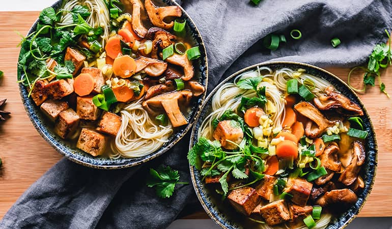 Two bowls filled with a vegetarian noodle dish featuring tofu and mushrooms