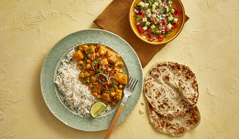 A bowl of Nadiya's Butternut Squash & Chickpea curry with flatbreads and salad